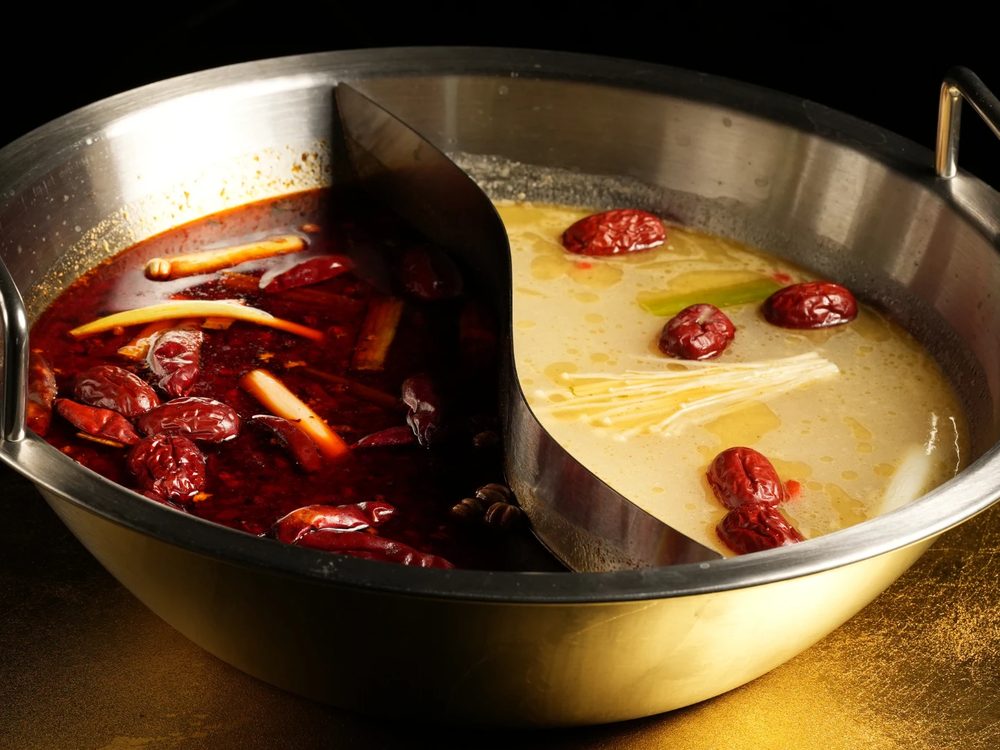 A divided hot pot, mala broth on one side and clear broth on the other