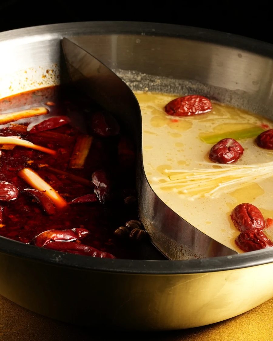 A divided hot pot with mala broth on one side and clear broth on the other