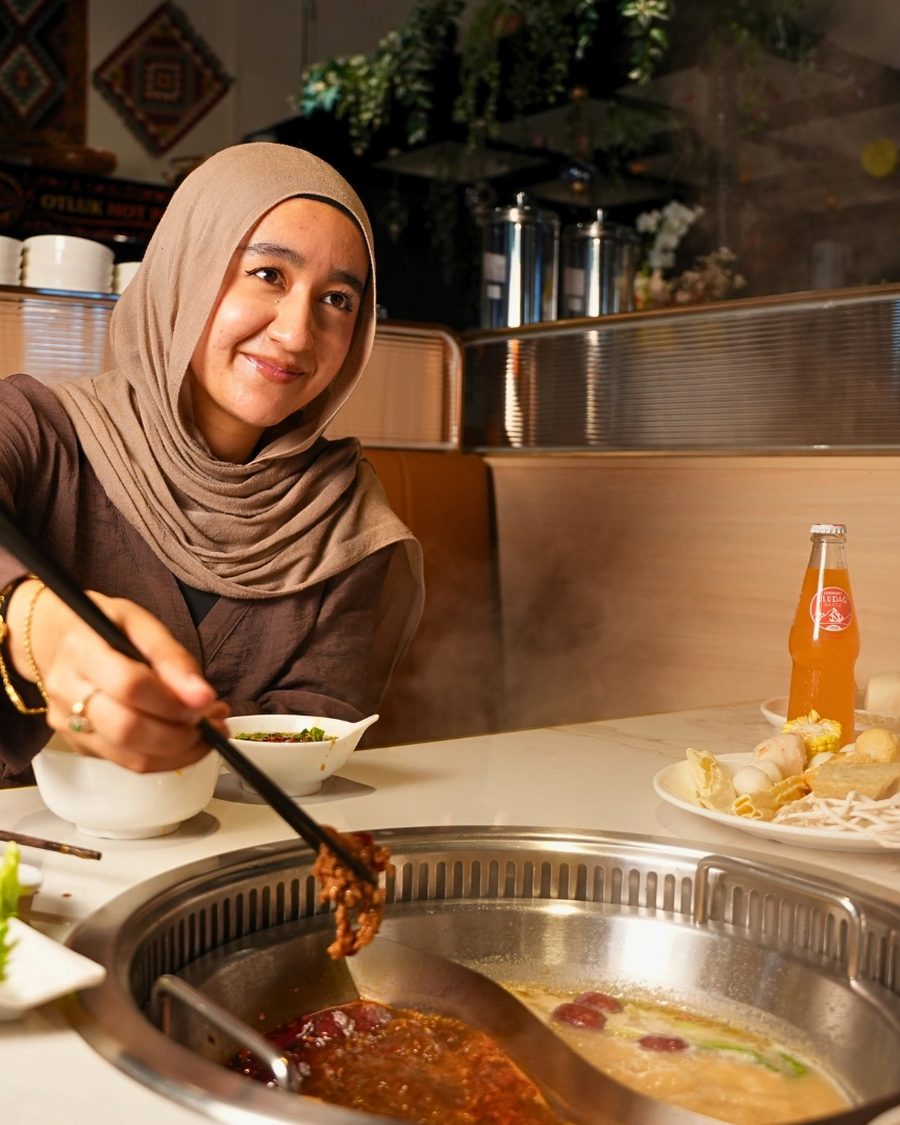A guest cooking sliced meat in a simmering broth at her table